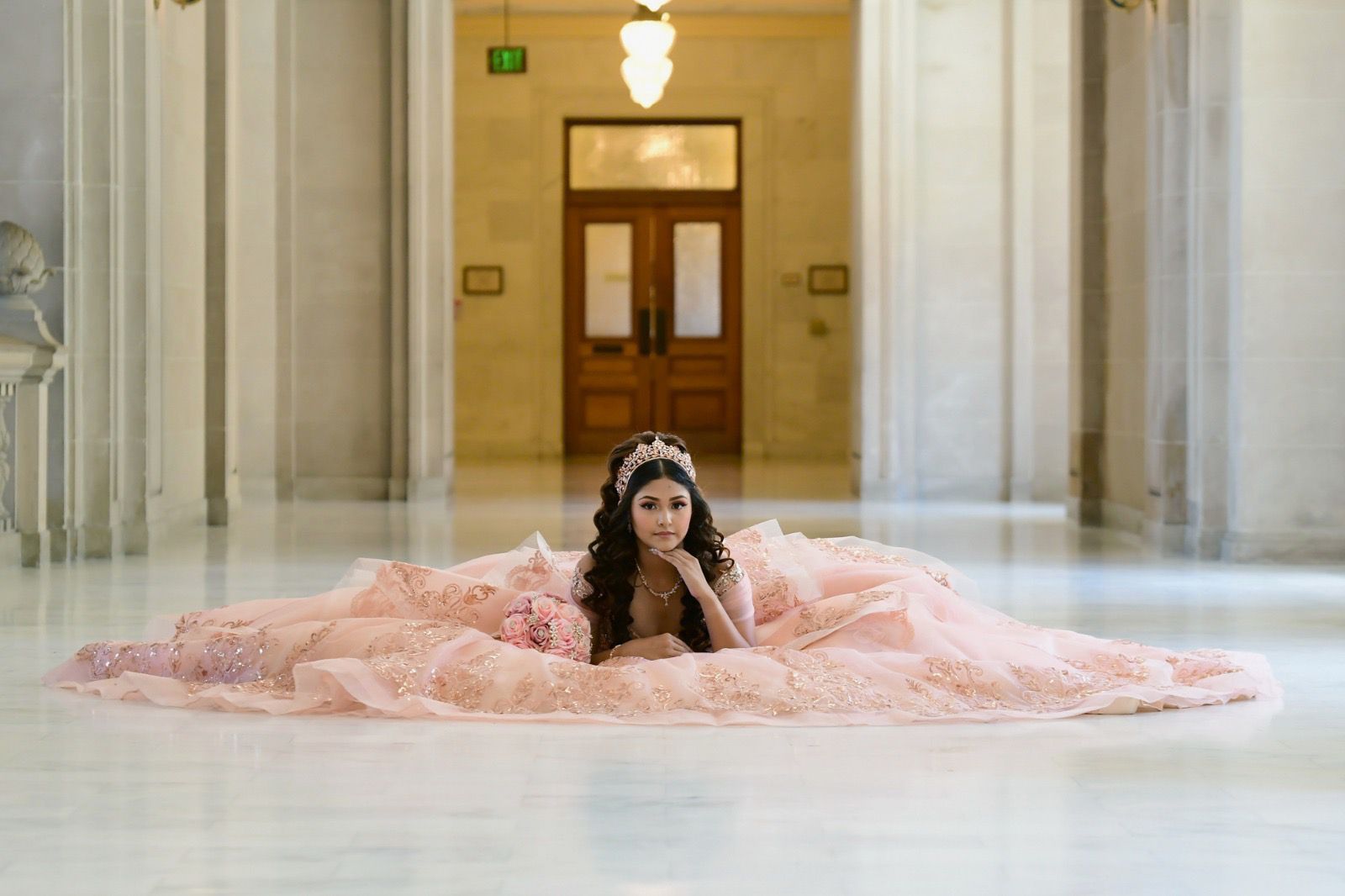 Quinceañera in pink gown lying in marble hallway