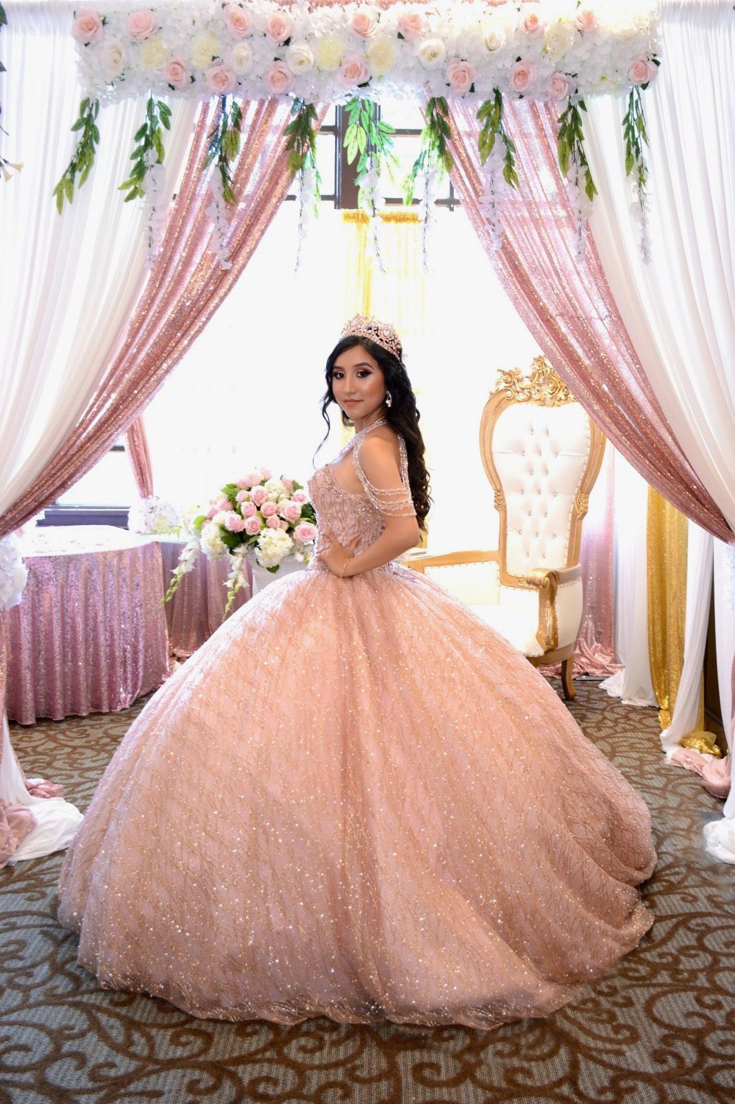 Quinceañera in pink ball gown at decorated throne backdrop